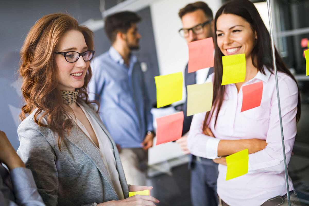 Female colleagues collaborate at work with postit notes on a clear window.