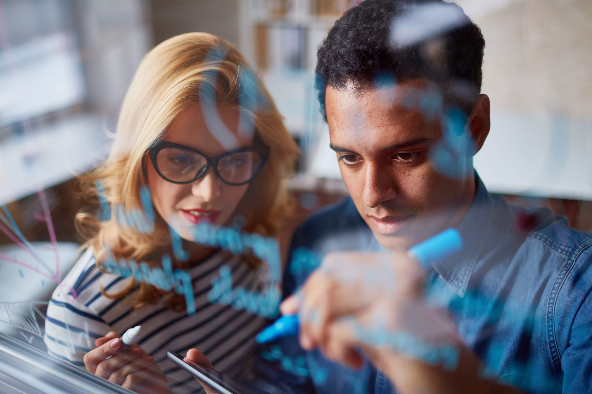 A man and women use a whiteboard and tablet together