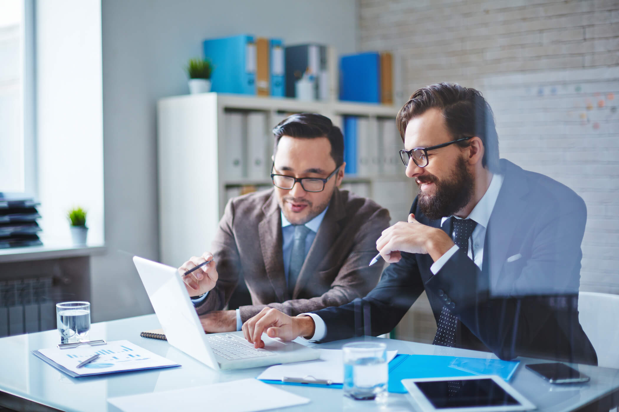 Two men in suits discuss and point to a laptop