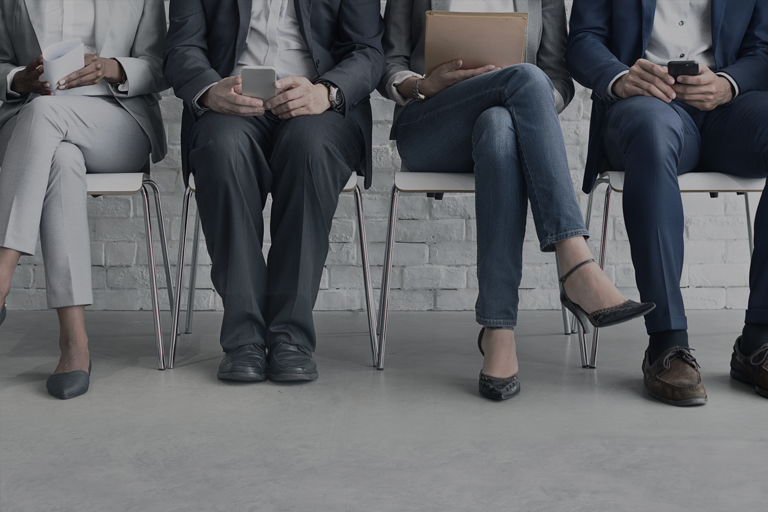 An assortment of people's legs as they sit in a clean, industrial looking reception area.